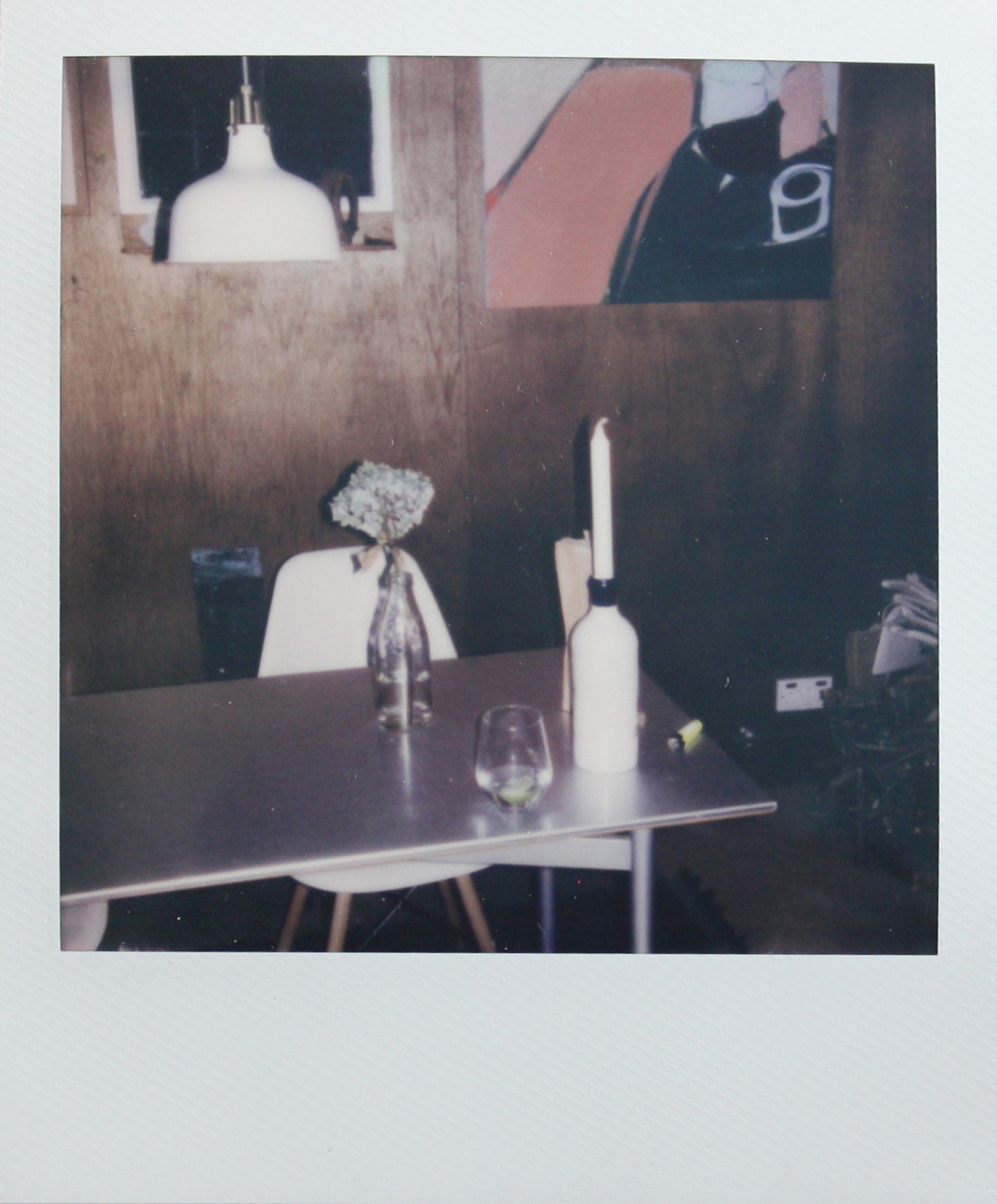 polaroid of a table with a candle in a bottle and a flower in a bottle