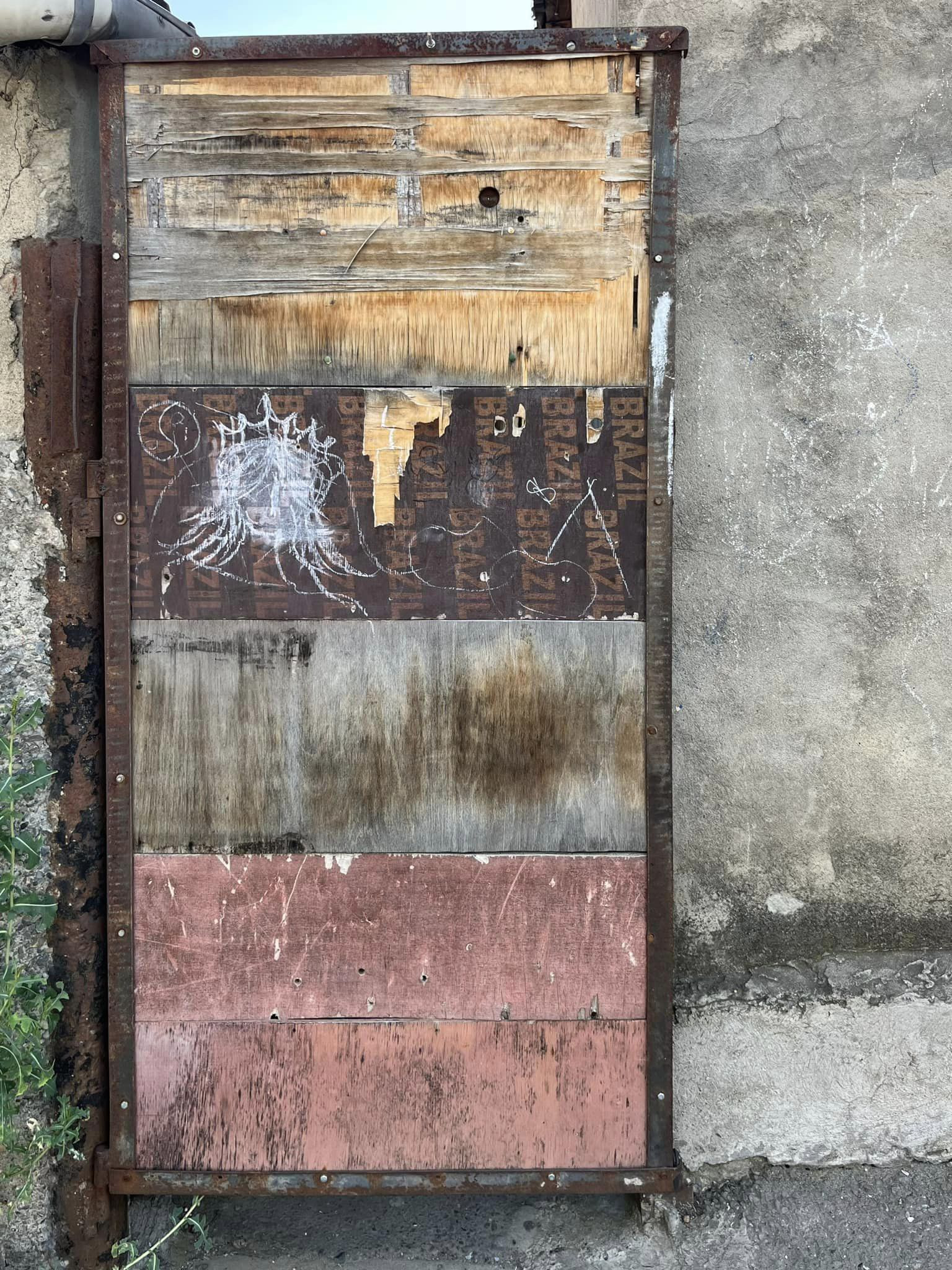 photo of a door made of horizontal boards with various peeling paint and drawings