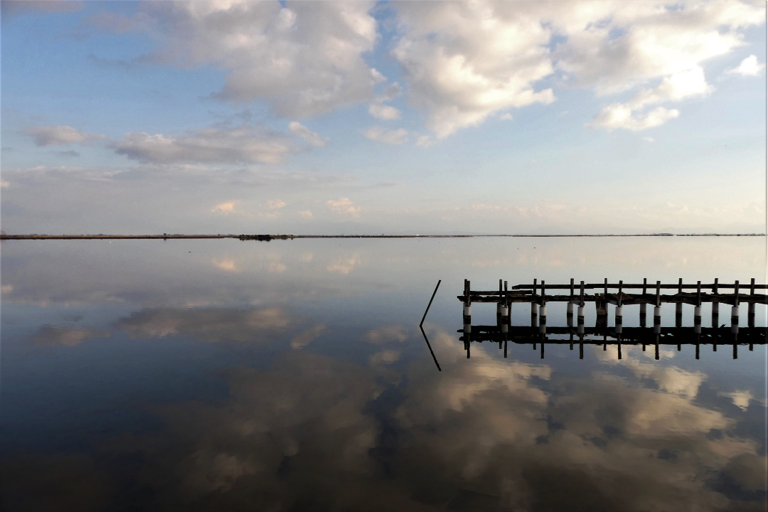 photograph of clouds and pier reflected in water at dusk