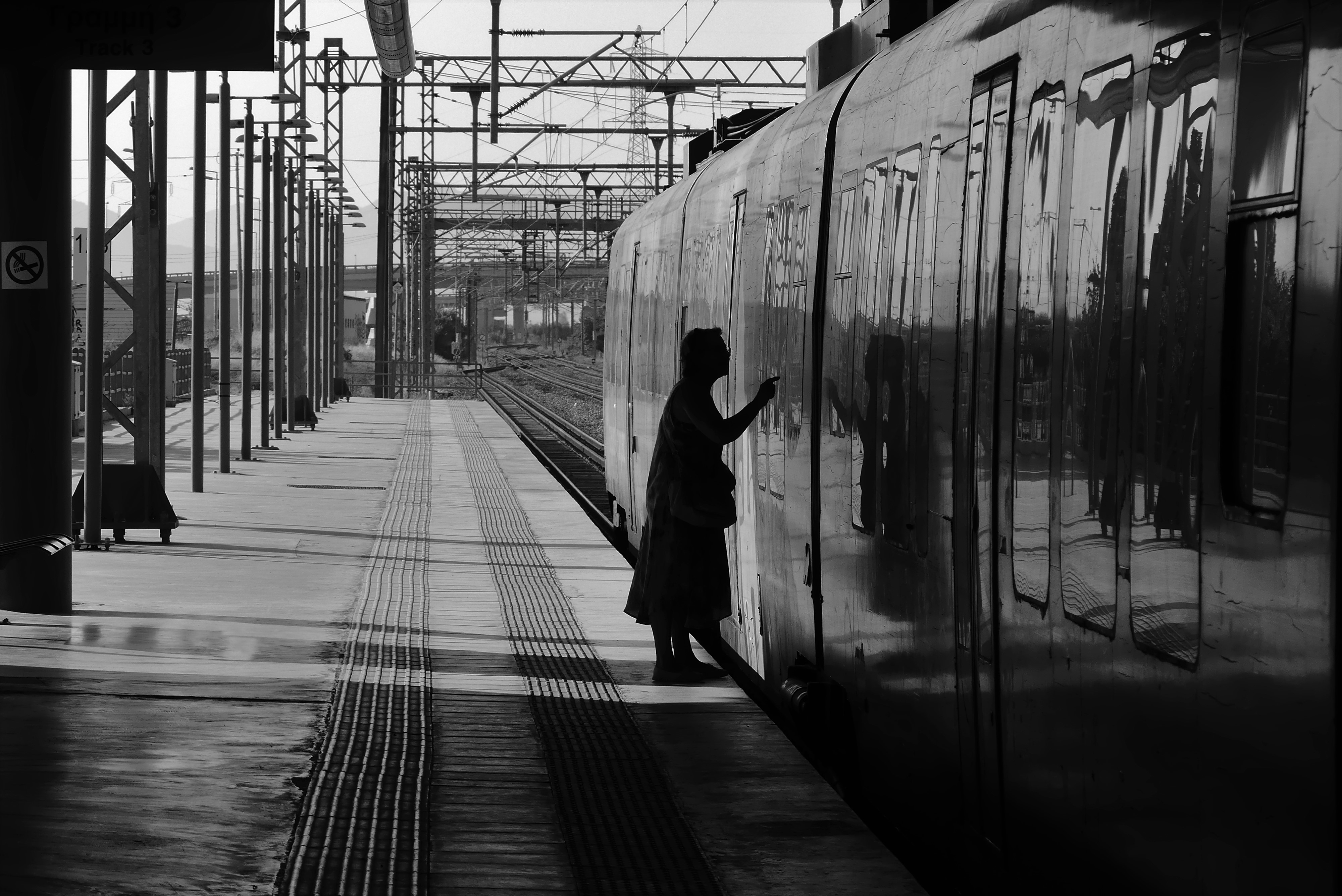 woman at train station with her hand up facing train on the tracks