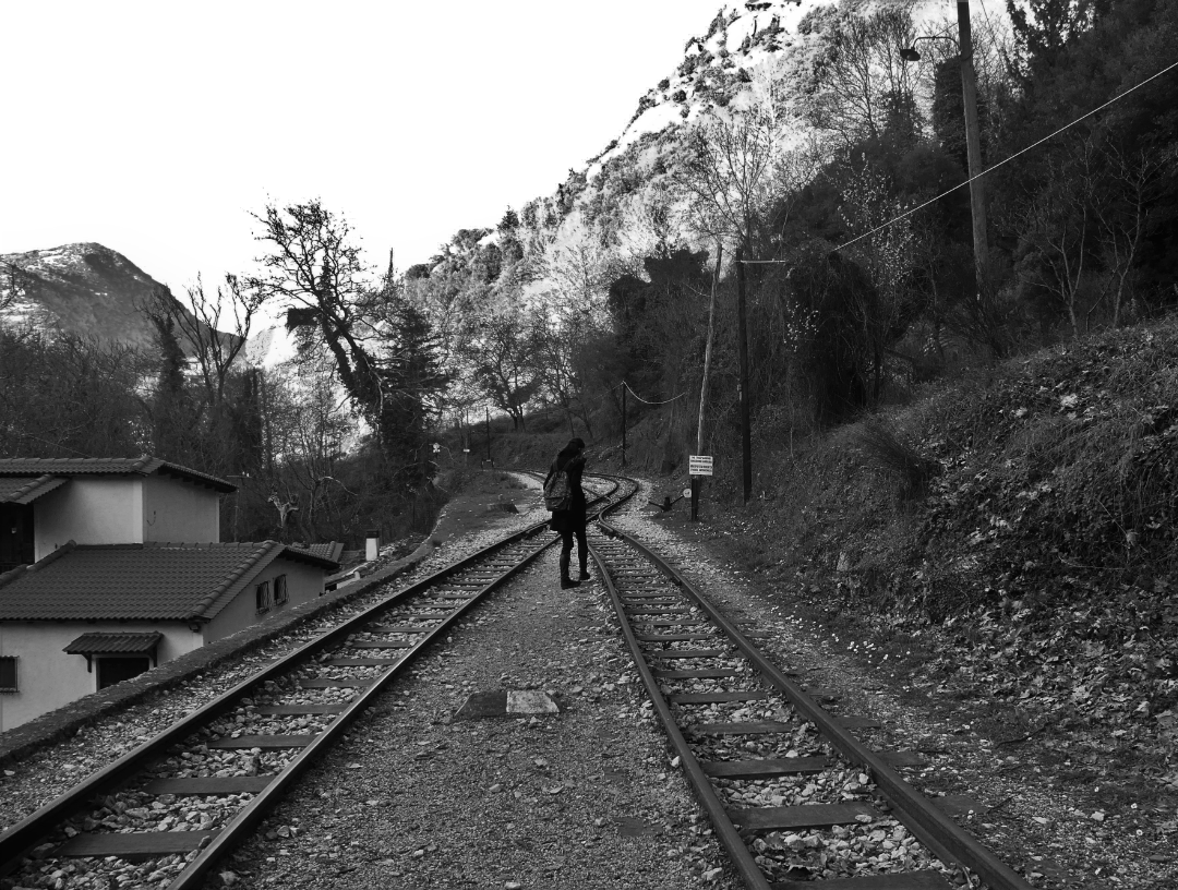 photograph from behind of young woman with backpack walking down train tracks